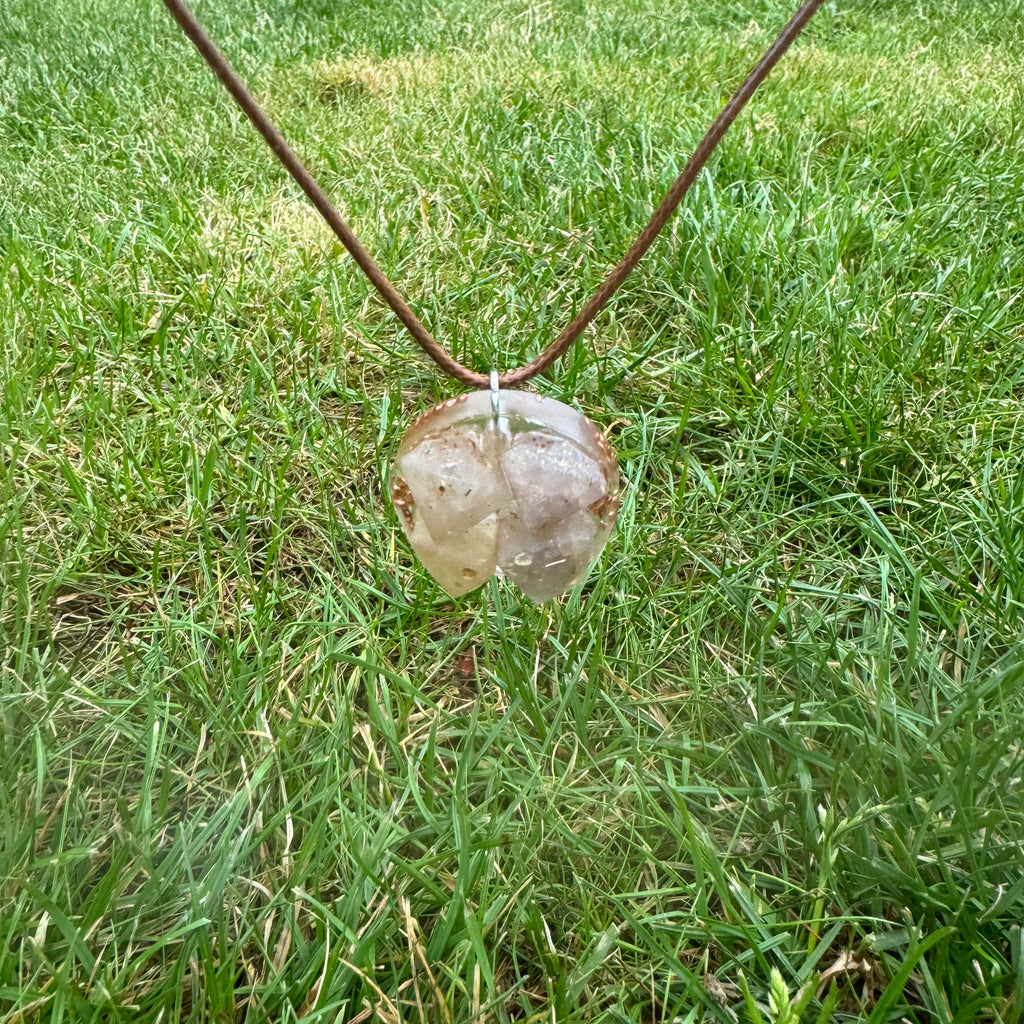 De Beta Kwarts & Koper ketting ligt zorgvuldig in gras, waarbij de heldere Beta Kwarts en koper glanzen in het zonlicht, symboliserend balans en kracht.