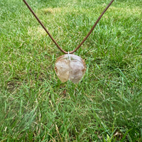 De Beta Kwarts & Koper ketting ligt zorgvuldig in gras, waarbij de heldere Beta Kwarts en koper glanzen in het zonlicht, symboliserend balans en kracht.