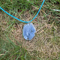 Een model draagt de handgemaakte Blauwe Calciet ketting, terwijl de ketting elegant zichtbaar is tegen de achtergrond van gras en natuurlijke omgeving.